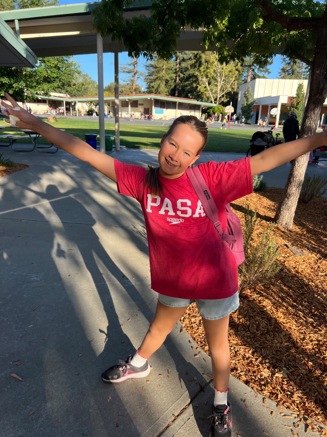 PASA swimmer in a red team shirt celebrating Pride Day with arms out wide on campus