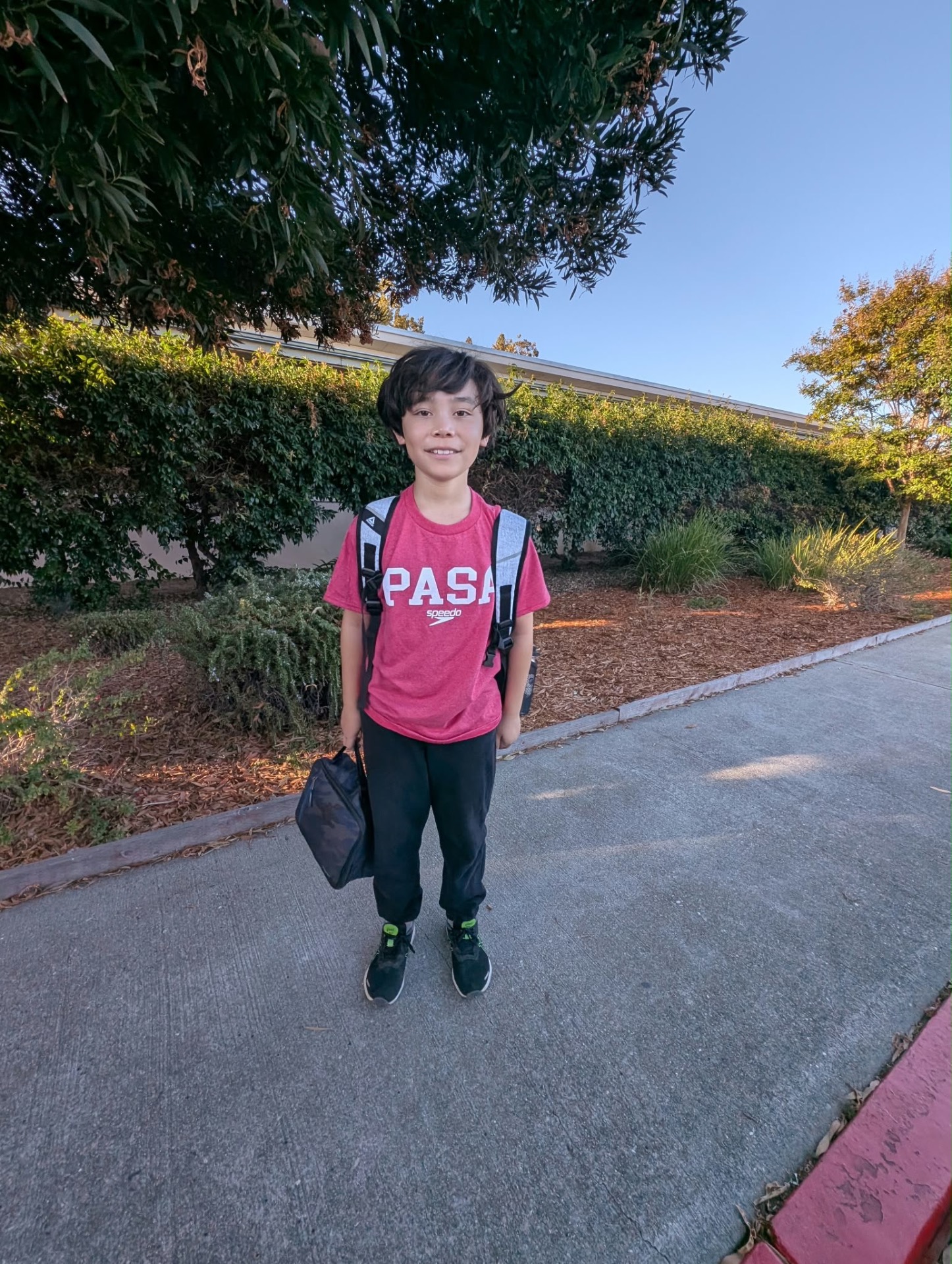 PASA swimmer in a red team shirt walking to school with backpack