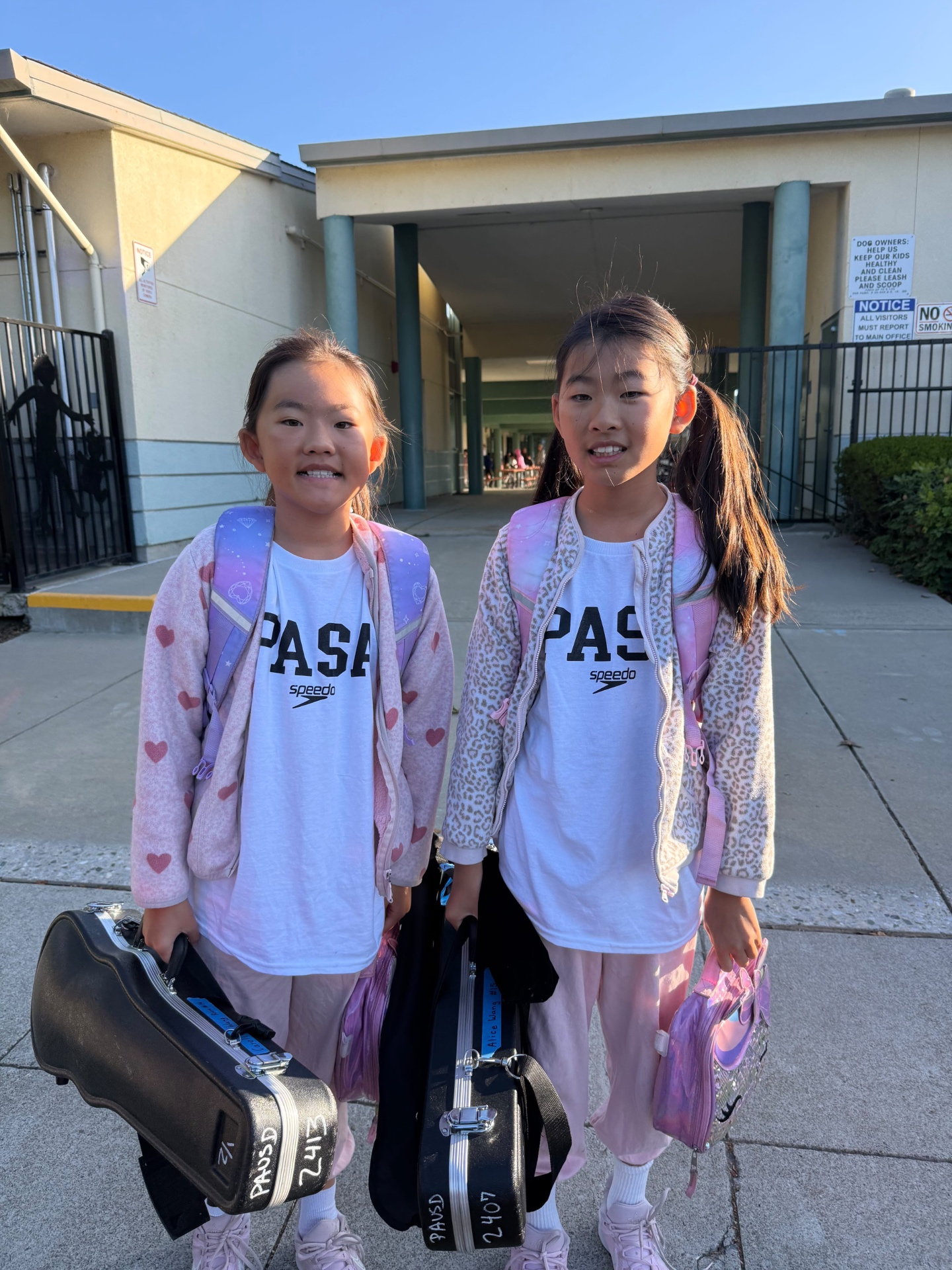 Two PASA swimmers in team shirts carrying their instruments to school