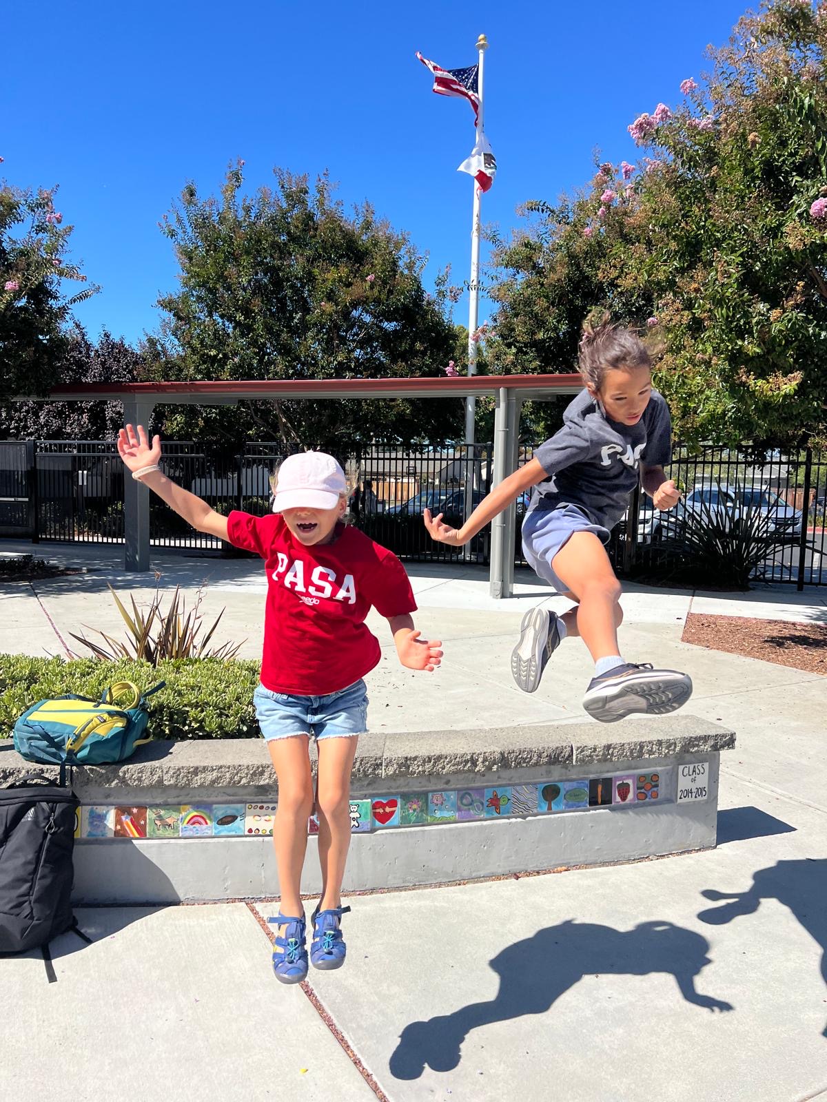 Two young PASA swimmers jumping for joy in team shirts on Pride Day